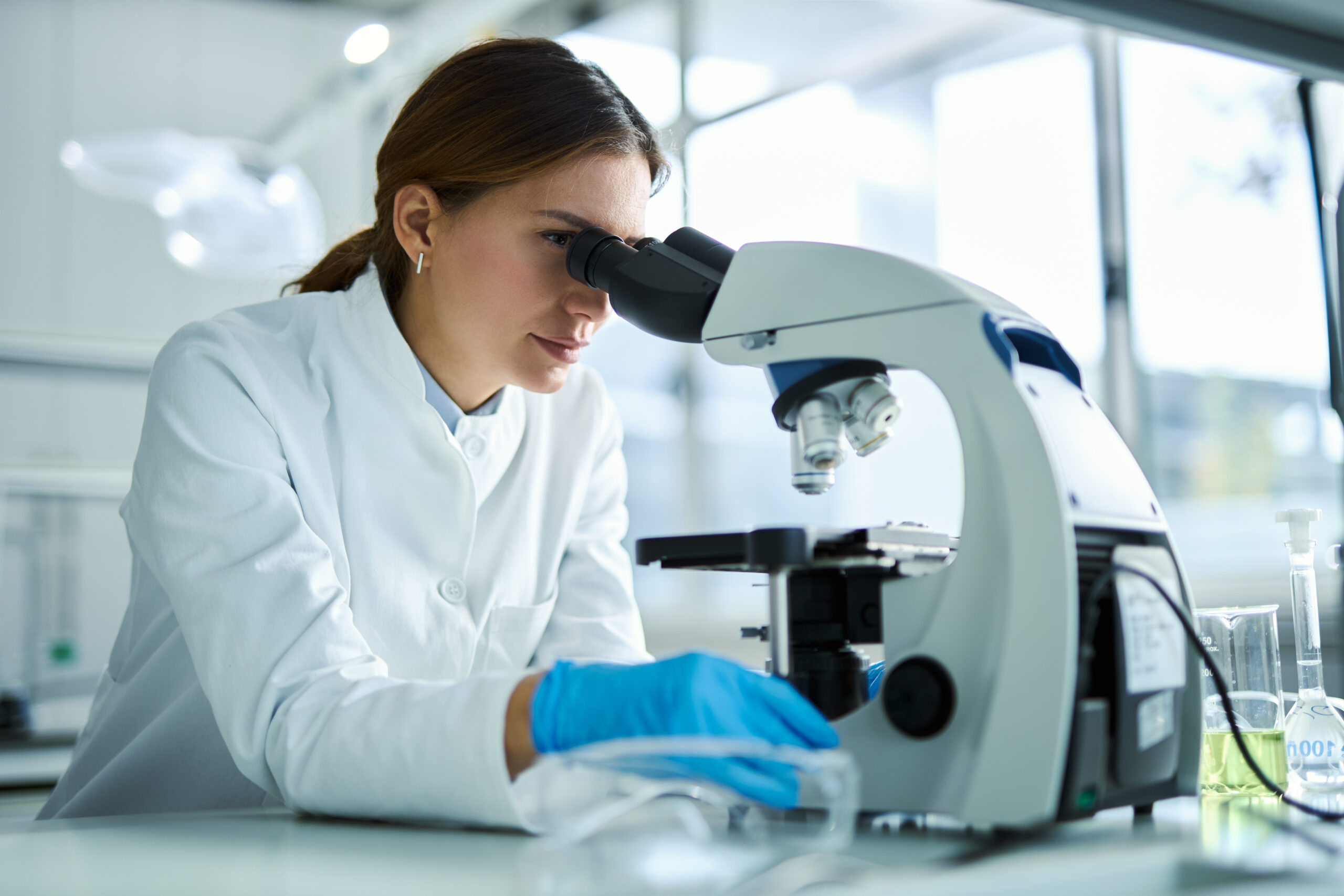 Young female scientist working on a research through a microscope in laboratory. Young female scientist working on a research through a microscope in laboratory.